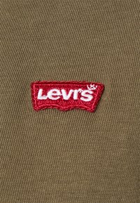 Wyszywane logo Levi's w kolorze czerwonym na khaki tle, z teksturowanym splotem i lekko wypukłym wzorem.
