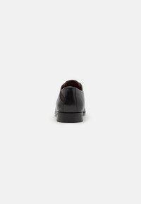Zapato de cuero negro con un acabado suave, diseñado con un tacón redondeado y detalles de costura mínimos, mostrando una silueta moderna y elegante.