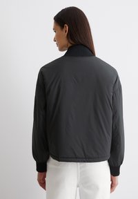 Schwarze Bomberjacke mit einem gerippten Kragen und Bündchen, aus einem glatten, leichten Material und mit einer taillierten Silhouette. Keine auffälligen Muster.