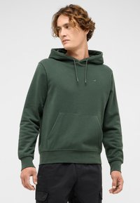 Zielona bluza z kapturem, z przednią kieszenią, kapturem ze sznurkiem i ściągaczami na rękawach. Wykonana z miękkiego materiału z subtelnym detalem w postaci logo.