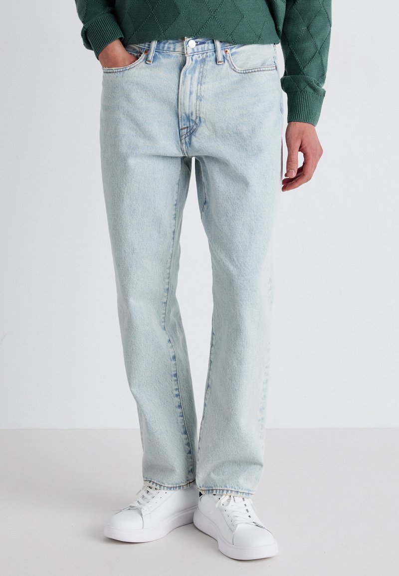 Lichtblauwe denim jeans met een rechte pasvorm, met subtiele vervaging, vijf-pocket ontwerp en een metalen knoopsluiting, gecombineerd met witte sneakers.