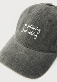 Grå baseballkasket i stof med broderet tekst "no planning just vibing" i hvid. Har buet skygge og seks-panel-konstruktion.