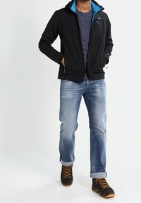 Black softshell jacket with blue accents, gray t-shirt, light denim jeans, and black boots with orange laces.