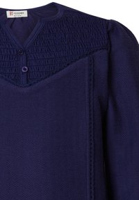 Mörkblå plagg med smockad ok, rund halsringning och två knappstängningar. Slät textur med dekorativ sömnadsdetaljer.