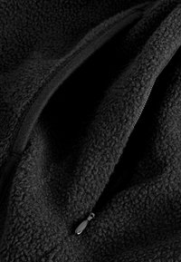 Tessuto di pile nero caratterizzato da una superficie texturizzata e un'apertura con zip dotata di un comodo tirazip, che mette in evidenza la morbidezza e il calore del materiale.