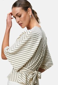 Cream top with black horizontal stripes, wrap-style design, flared sleeves, and a tied back. Textured fabric with a lightweight appearance.