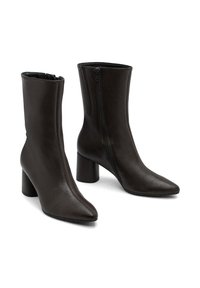 Un par de botas de cuero marrón oscuro hasta el tobillo con puntas afiladas, cremalleras laterales y tacones anchos.