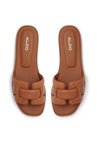 Sandales à glissière beiges avec une large sangle rembourrée, ornée d'un design de boucles décoratives. Texture en cuir lisse ; semelle plate, design minimaliste.