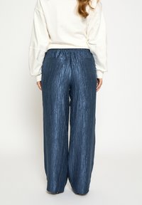 Wijde broekspijpen in een glanzende, getextureerde donkerblauwe stof. Voorzien van een elastische tailleband en eenvoudige achterzakken.