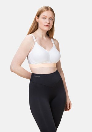 Weißer Sport-BH aus strukturiertem Stoff mit verstellbaren Trägern, kombiniert mit hochgeschnittenen schwarzen Leggings, die ein Logo am Bund aufweisen.