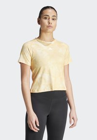 Maglietta atletica a maniche corte, corta, di colore giallo pastello con motivo tie-dye e scollo rotondo, con un branding sottile sul petto.