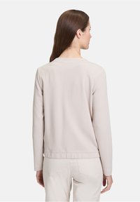 Gilet texturé beige clair avec un col rond et des manches longues. Présente un design simple et épuré sans matériel visible.
