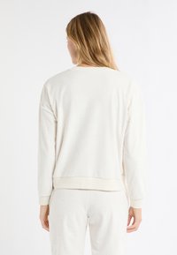 Kremowa bluza z wzorem w gwiazdy, okrągłym dekoltem i ściągaczami przy rękawach. Miękka w dotyku, o luźnym kroju, pokazana od tyłu.