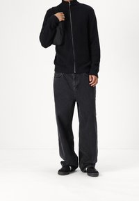 Svart ribbad stickad zip-up jacka, kombinerad med löst sittande svarta denimjeans. Accessoar: liten svart väska. Fotwear: svarta skor.