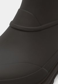 Musta kumikenkä, jossa on sileä pinta, pyöreä kärki ja pyöreä koriste ylhäällä. Suunnittelussa on yksinkertainen ja toiminnallinen muoto.