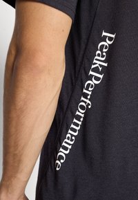 Close-up of an arm next to a black shirt with white vertical text reading "Peak Performance" along the side seam.