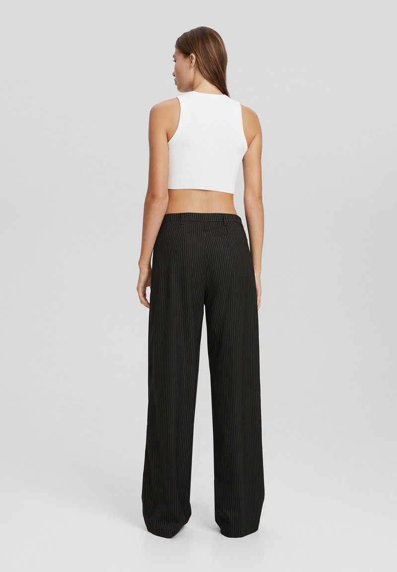 Un haut court côtelé blanc associé à un pantalon large à rayures fines noir à taille haute. Coutures visibles et texture lisse sur les deux vêtements.