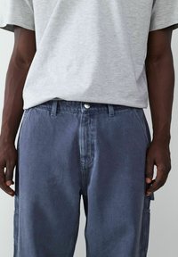 Szary t-shirt w połączeniu z luźnymi, ciemnoniebieskimi spodniami typu cargo z denimu, które mają boczne kieszenie i guzik w pasie.