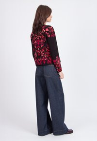 Suéter negro con un patrón floral rojo, combinado con unos jeans de mezclilla oscura de pierna ancha. El conjunto cuenta con mangas largas y un corte relajado.
