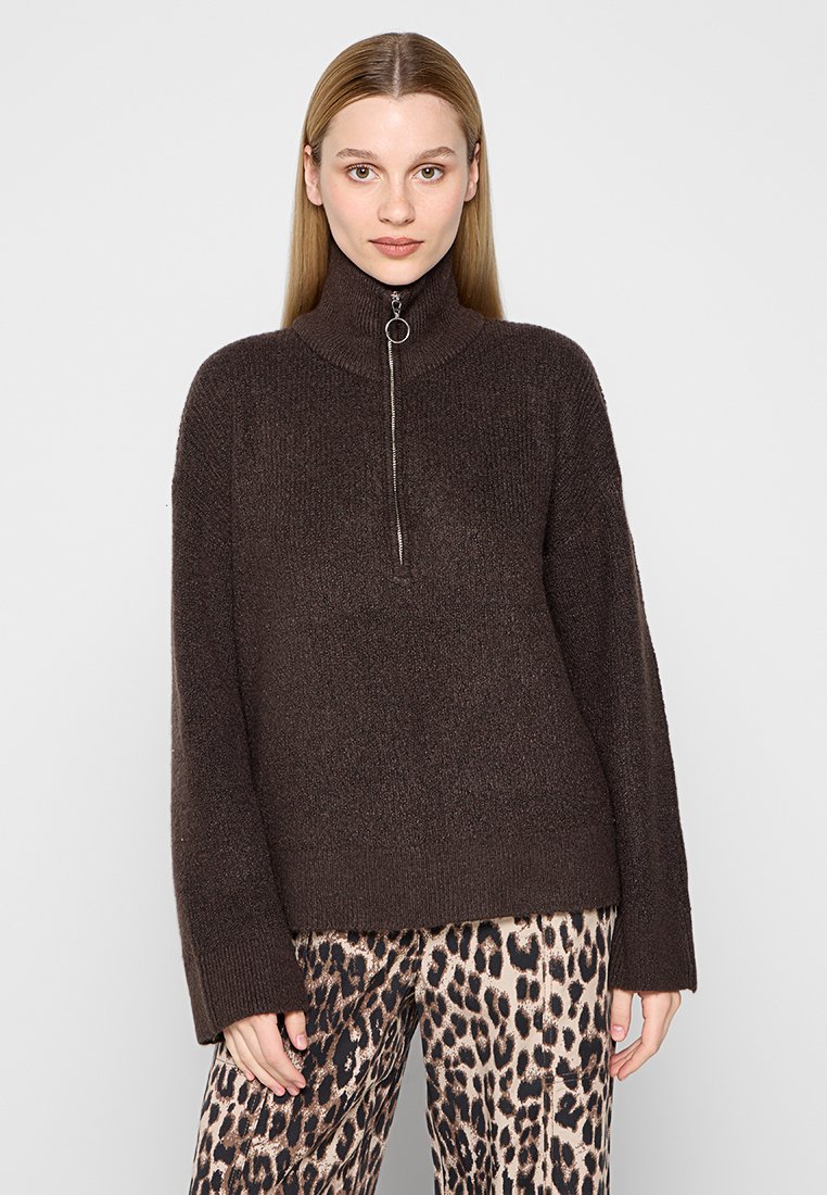 Brauner Strickpullover mit hohem Kragen und silbernem Reißverschluss, kombiniert mit Hosen im Leopardenmuster. Weicher Stoff und lässige Passform.