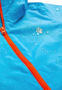 Wodoodporna niebieska kurtka z pomarańczowym suwakiem. Posiada krople na powierzchni oraz małe srebrne logo na piersi.