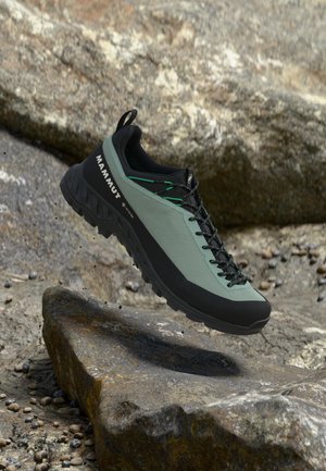 Grøn og sort Mammut vandresko med Gore-Tex, vist over klippefyldt udendørs terræn, der fremhæver robust sål og snøredetaljer.