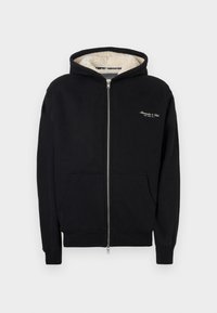 Veste à capuche zippée noire en tissu doux, avec une capuche doublée en polaire, des poches avant et un logo brodé blanc sur la poitrine.