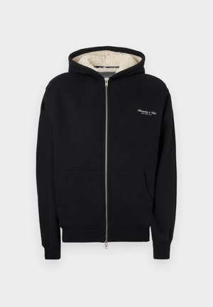 Svart zip-up hoodie i mjuk tyg, med fleecefodrad huva, framfickor och vit broderad logotyp på bröstet.
