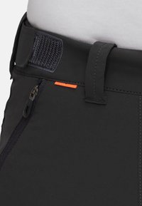 Sorte bukser med tekstureret stof, der har en diagonalt lynlåslomme og en orange detalje nær taljen; sikret med en velcro-lukning.
