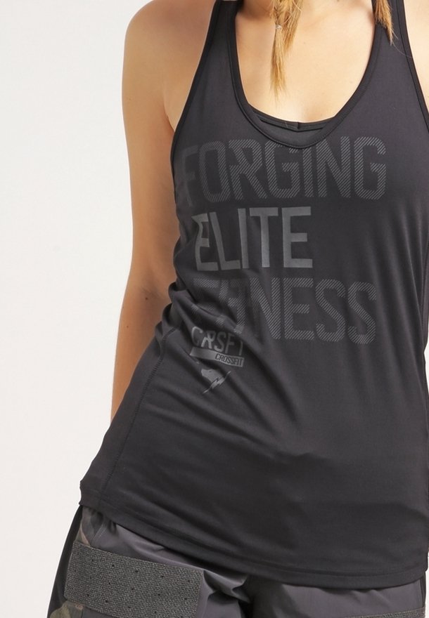 Femme portant un haut de sport noir sans manches avec le texte "Forging Elite Fitness" et un short de sport gris avec une fermeture velcro.