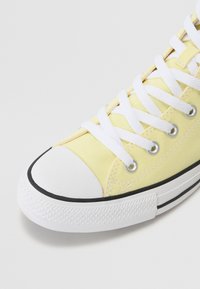 Gelbe Leinensneaker mit weißen Schnürsenkeln, schwarzer Gummisohle und weißer Zehenkappe. Verfügt über metallische Ösen und eine strukturierten Gummisohle.