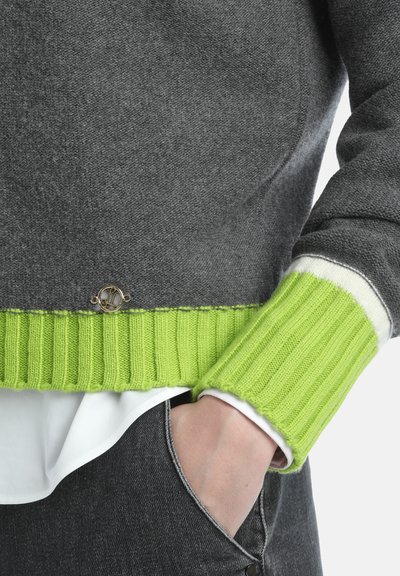 Pull gris avec un ourlet et des poignets côtelés en vert citron, avec un accent blanc. Détail en métal doré près de l'ourlet. Tissu doux et texturé.