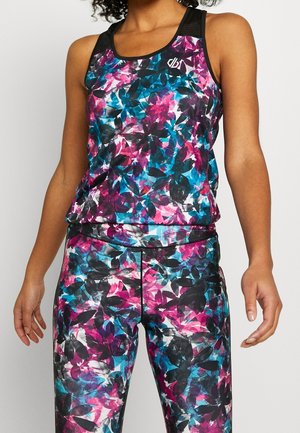 Kobieta ubrana w kolorowy sportowy tank top w kwiatowy wzór oraz dopasowane legginsy w czarnych, niebieskich, różowych i fioletowych odcieniach na jednolitym tle.