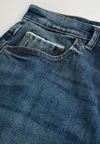 Ciemnoniebieskie dżinsy z denimu o klasycznym kroju, z widoczną tylną kieszenią i srebrnymi elementami metalowymi. Miękki, fakturowany materiał.