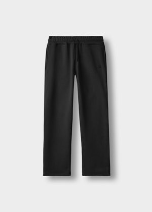 Pantalons de survêtement noirs à jambe droite avec taille élastique, cordon de serrage, poches latérales et logo discret sur la cuisse gauche, présentés sur fond blanc.