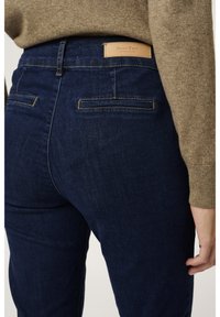 Jean en denim bleu à taille haute avec des poches arrière. Dispose d'une étiquette en cuir beige à la taille avec l'inscription "Part Two" embossée.