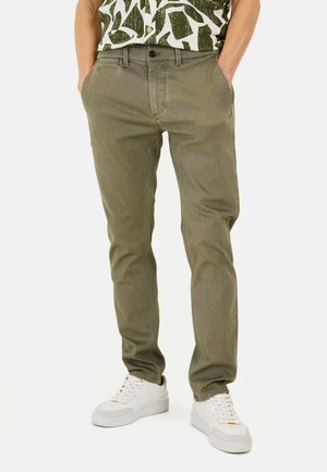 Khaki chinos met een getailleerd ontwerp, gemaakt van katoen, met zijzakken, een ritsgulp en subtiele stikdetails, gecombineerd met witte sneakers.