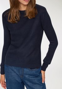 Granatowy sweter dzianinowy z okrągłym dekoltem i długimi rękawami, z prążkowanymi mankietami i dołem, w zestawieniu z niebieskimi dżinsami.