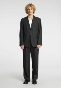 Czarna marynarka i spodnie o dopasowanym kroju, z klapami z wycięciami, dwoma guzikami i bocznymi kieszeniami, noszone na białej koszuli.