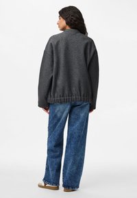 Maglione grigio over-size con finitura texturizzata, dotato di orlo a coste e spalle scese, abbinato a jeans blue a gamba larga e scarpe beige.