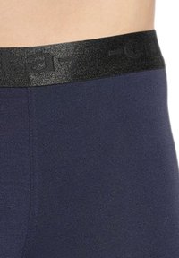 Navy blue leggings with a textured black elastic waistband featuring a logo, smooth fabric, and form-fitting design.