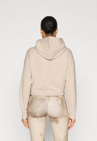 Μπεζ κοντό φούτερ με κουκούλα και κορδόνι, καθώς και ελαστική τελική ραφή, συνδυασμένο με ανοιχτό μπεζ κολάν με κηλίδες υφής και ραφές λεπτομερειών.