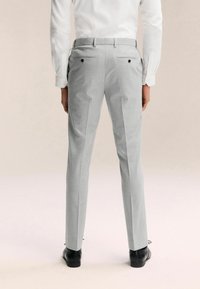 Graue maßgeschneiderte Hose mit Slim-Fit, ausgestattet mit zwei Gesäßtaschen und dezenten Seitennähten, kombiniert mit schwarzen eleganten Schuhen.