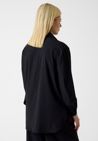 Zwart langermig shirt met een relaxte pasvorm, geruite manchetten en een gebogen zoom, gemaakt van een gladde, lichtgewicht stof.