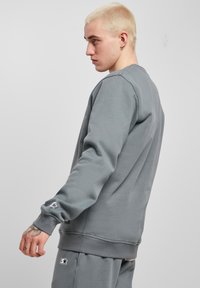 Felpa grigia con scollo rotondo e polsini a coste, con un logo discreto sulla manica e una vestibilità comoda. Texture liscia.