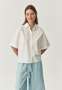 Camicia bianca a maniche corte con colletto. Abbinata a pantaloni larghi di colore azzurro chiaro. Design semplice e pulito.