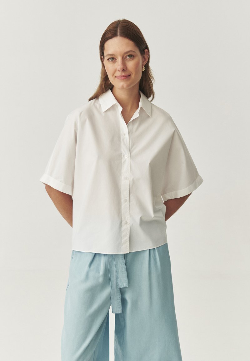 Camicia bianca a maniche corte con colletto. Abbinata a pantaloni larghi di colore azzurro chiaro. Design semplice e pulito.