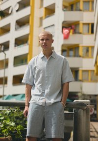 Camicia a maniche corte a righe blu e bianche con colletto e bottoni, abbinata a pantaloni corti a righe coordinati. Presenta una vestibilità rilassata.