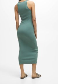 Vestido midi ajustado sin mangas en suave tela de color teal con una textura lisa y una abertura lateral, combinado con sandalias de color marrón claro.
