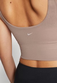 Sutien desportivo listrado em castanho claro com decote redondo e o logo da Nike em branco. Material texturizado e design ajustado para conforto.